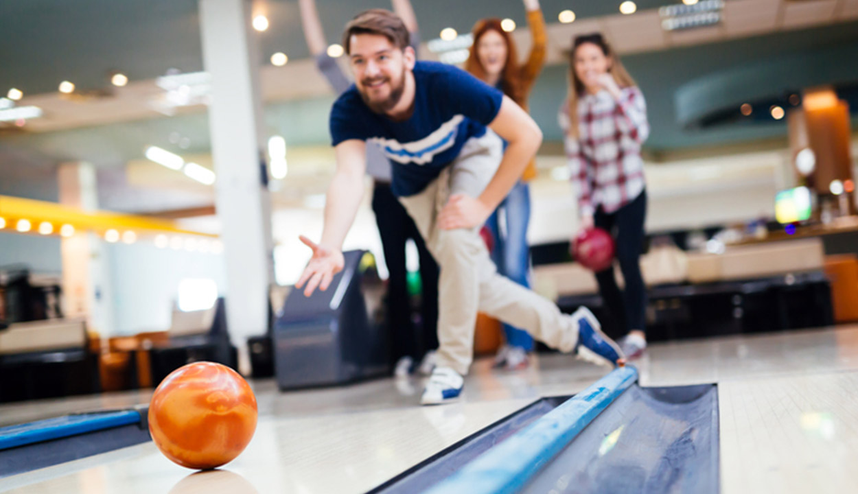 young adult bowling an orange ball down the lane during a team building exercise