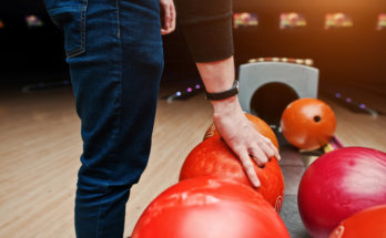 person picking up a red bowling ball
