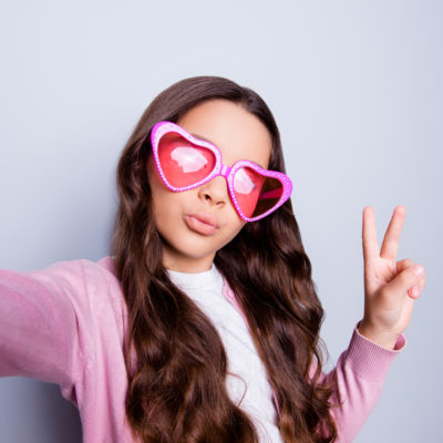 Tween girl taking a selfie while making peace sign and heart-shaped sunglasses