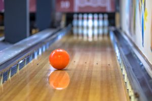 orange bowling ball curving as it goes down the alley towards the pins
